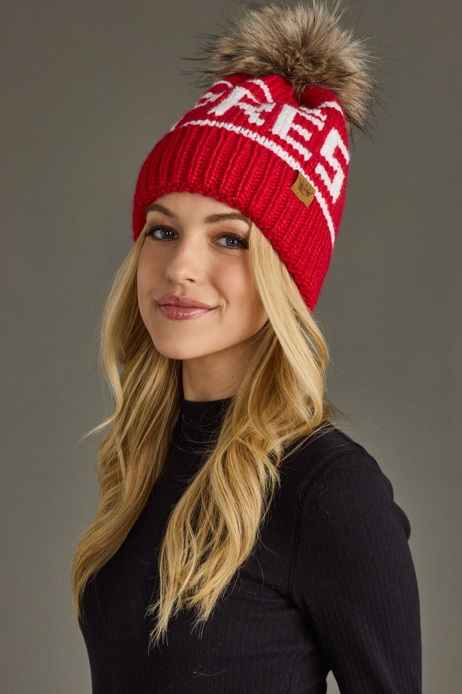 Woman wearing a red knit hat with a fur pom-pom against a gray background