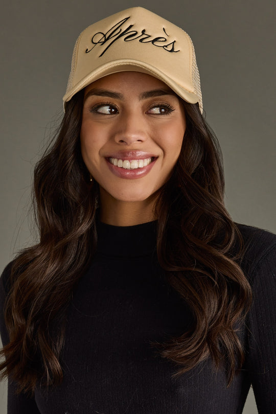 Woman wearing a beige cap with 'Apres' text against a gray background