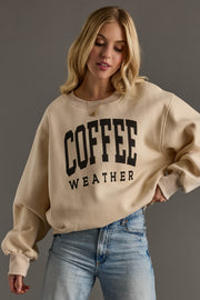 Woman wearing a beige sweatshirt with 'COFFEE WEATHER' text against a gray background