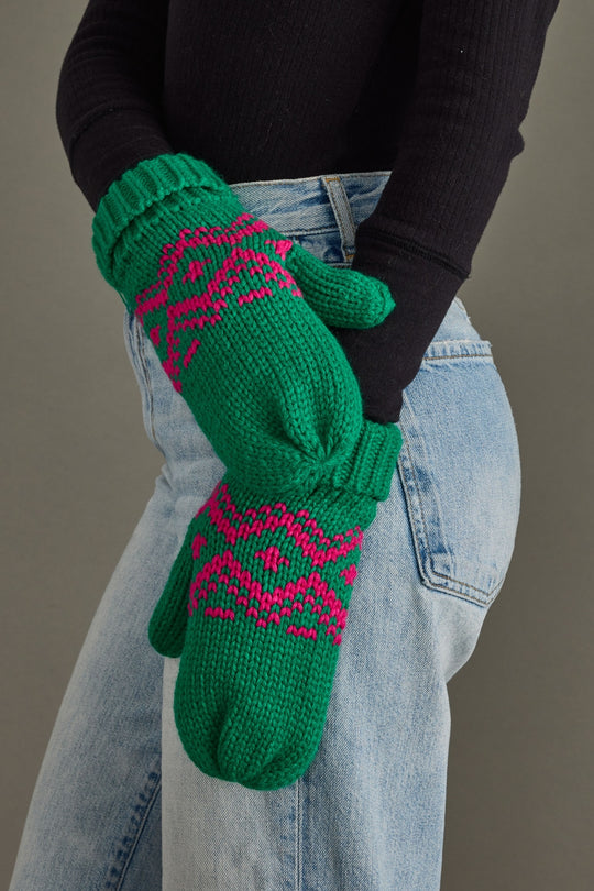 Green mittens with pink patterns worn by a person against a neutral background