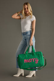 Woman holding a green bag with 'merry' written on it against a gray background