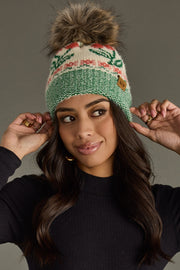 Woman wearing a green and beige knitted beanie with a pom-pom against a gray background