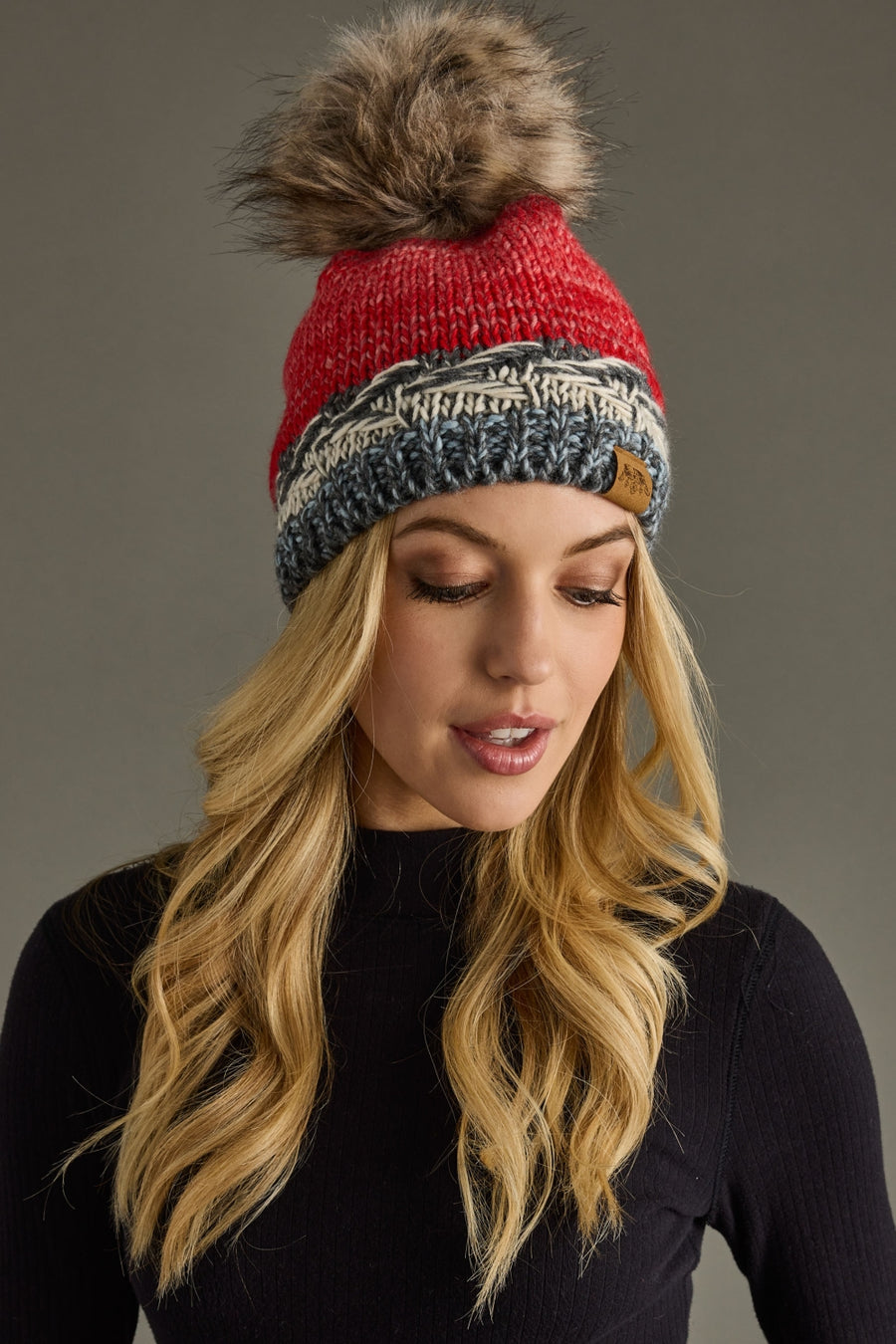 Woman wearing a colorful knit beanie with a pom-pom on a gray background