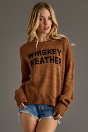 A cozy camel-brown knit sweater featuring bold black “Whiskey Weather” lettering across the front for a playful, seasonal statement. Designed with a relaxed fit, soft textured knit, and a classic crew neckline, this sweater offers all-day comfort with an effortlessly casual feel. Finished with long sleeves and ribbed cuffs and hem, it’s perfect for layering through cool fall days and pairing with your favorite denim.