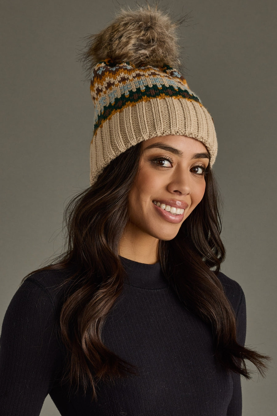 Woman wearing a beanie with a fur pom-pom against a gray background