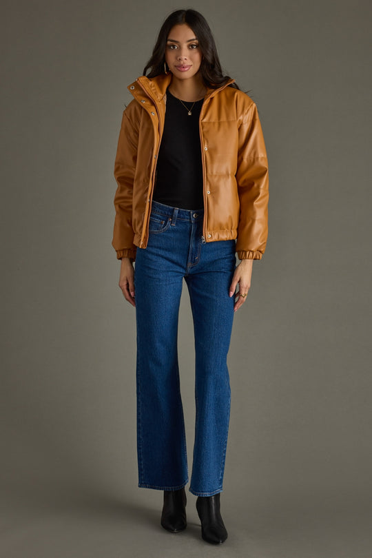 Woman wearing a brown leather jacket and blue jeans against a gray background