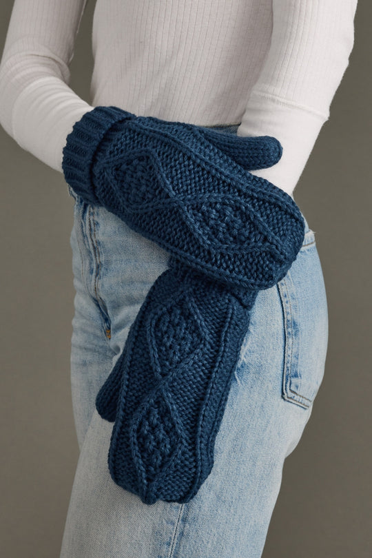 Blue knitted gloves worn by a person with a neutral background