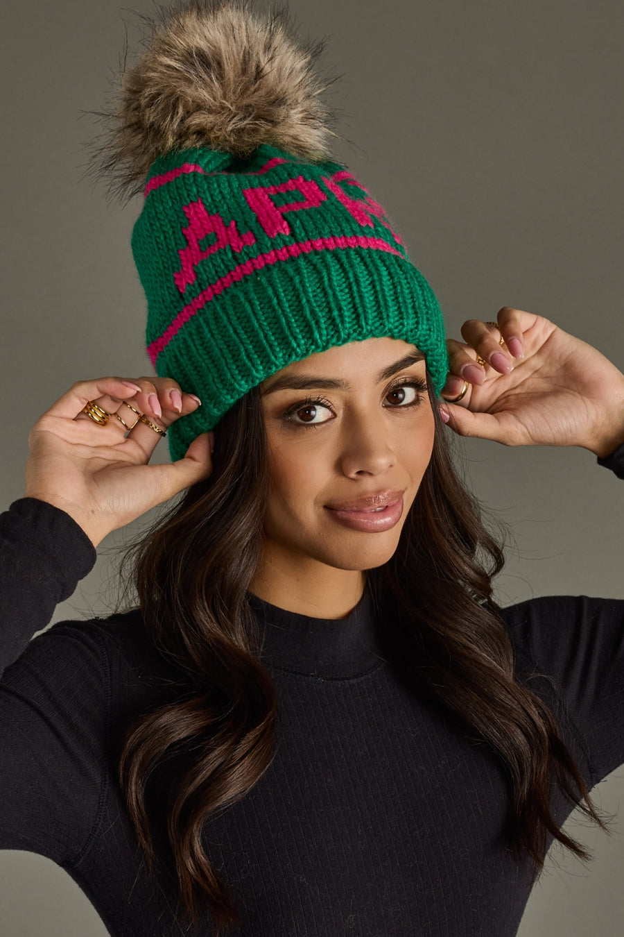Woman wearing a green beanie with a pom-pom, posing against a neutral background