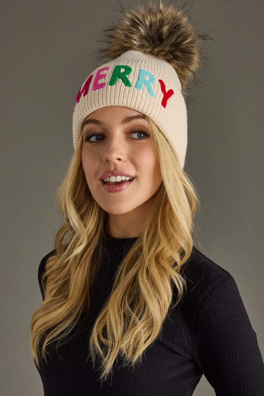Woman wearing a cream beanie with colorful letters on a gray background