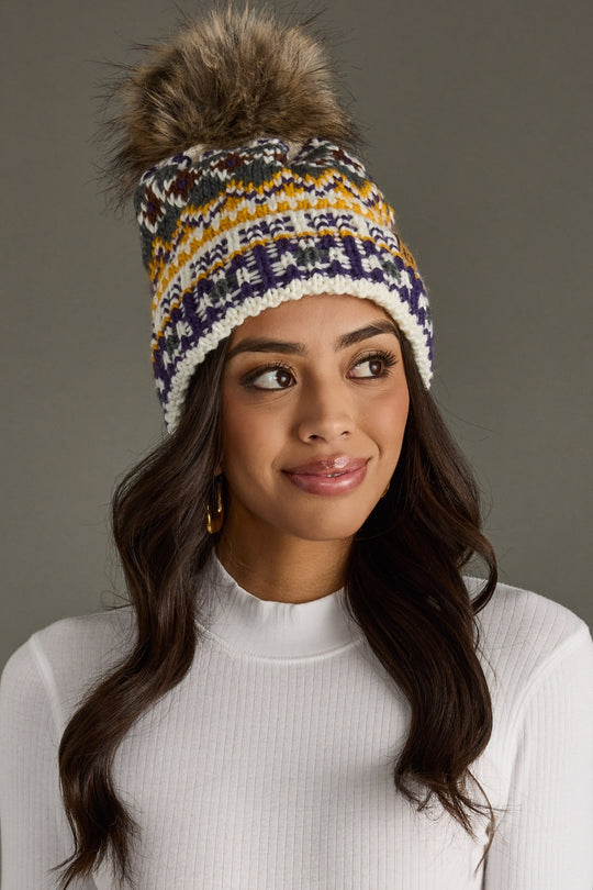 Woman wearing a colorful knit beanie with a fur pom-pom on a gray background