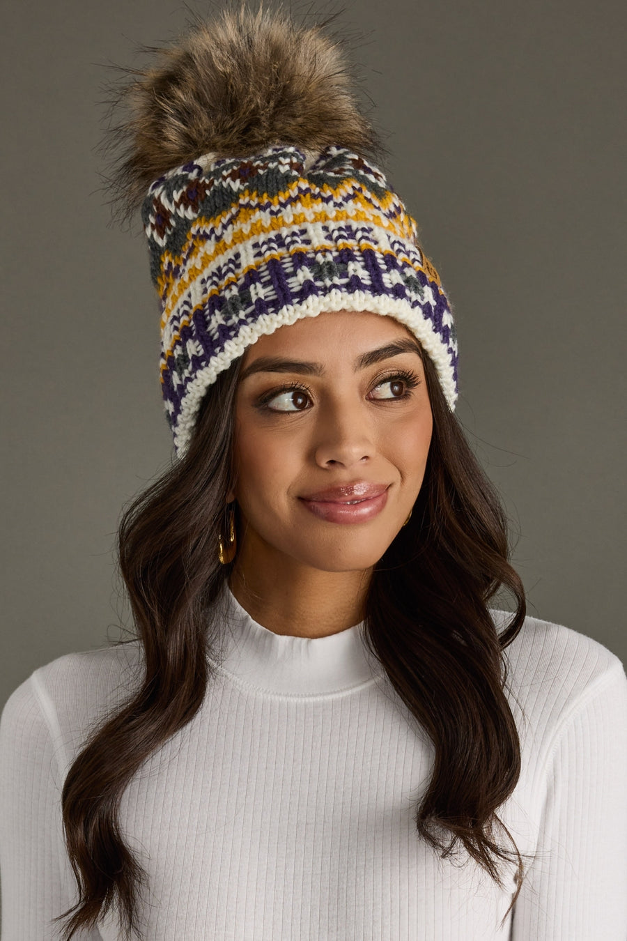 Woman wearing a colorful knit beanie with a fur pom-pom on a gray background