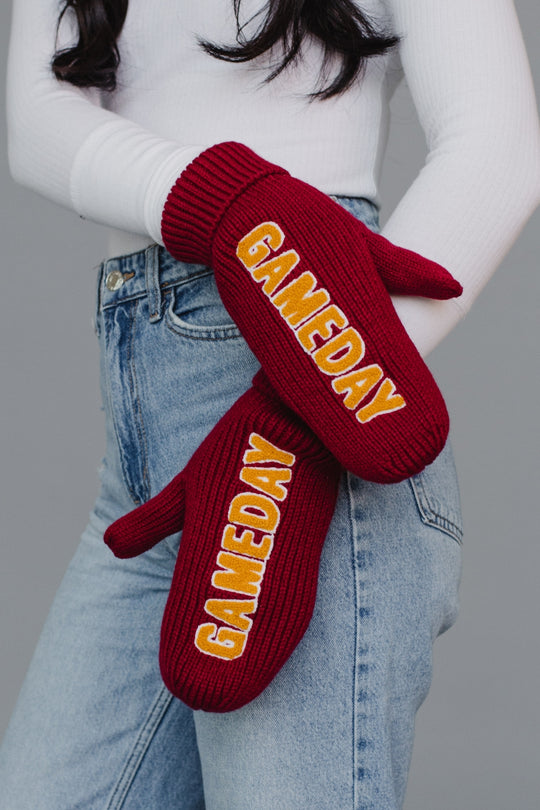 Red 'GAMEDAY' mittens worn by a person against a gray background
