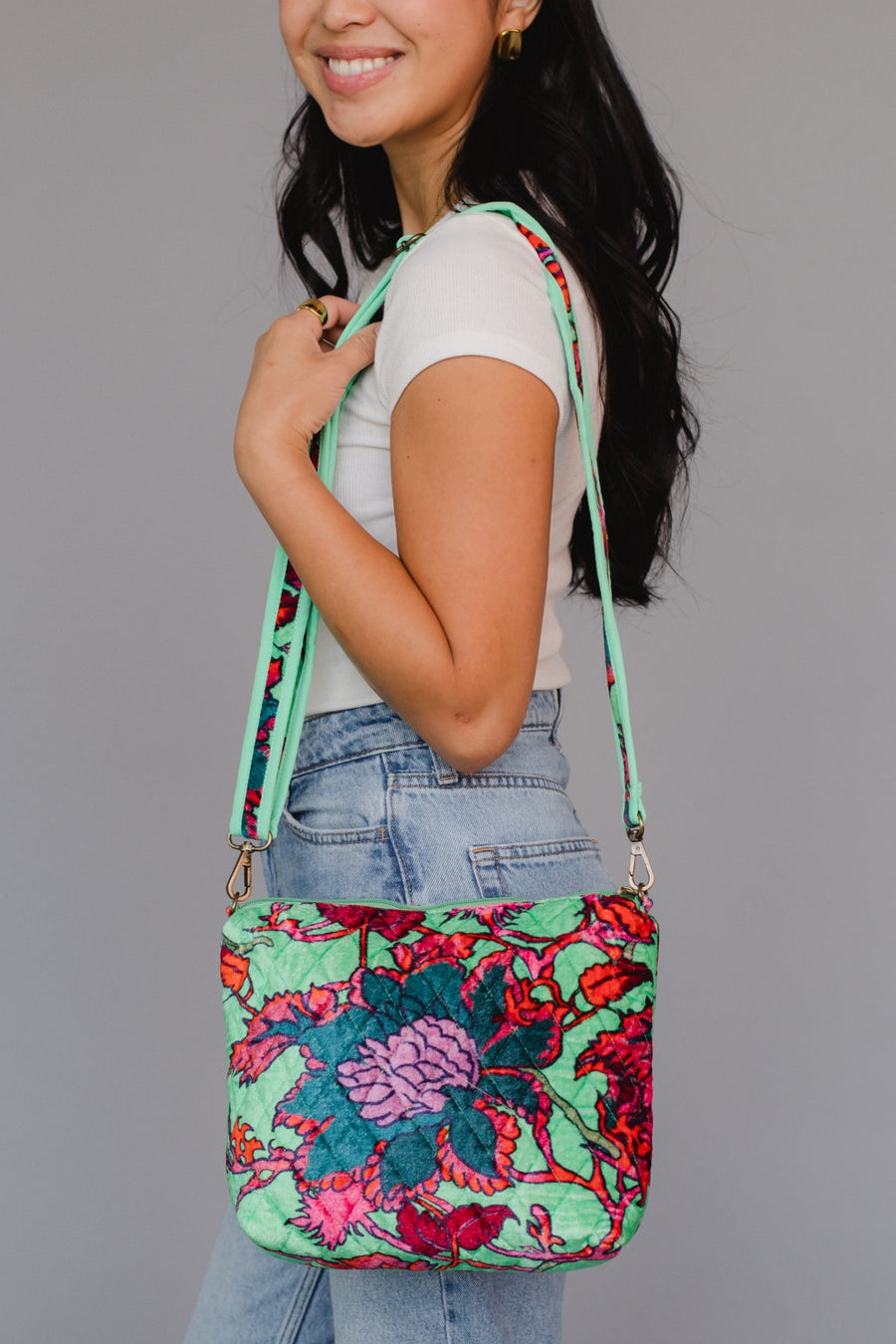 Woman holding a colorful floral-patterned crossbody bag against a gray background