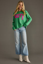Woman wearing a green sweater with pink text and blue jeans on a gray background
