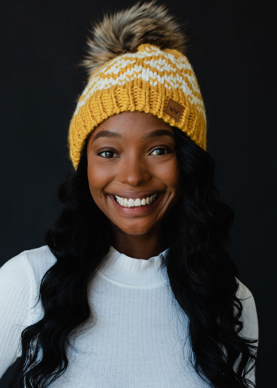 Woman wearing a yellow knit beanie with a pom-pom against a black background