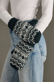 Person wearing dark teal and white patterned mittens with a plain background