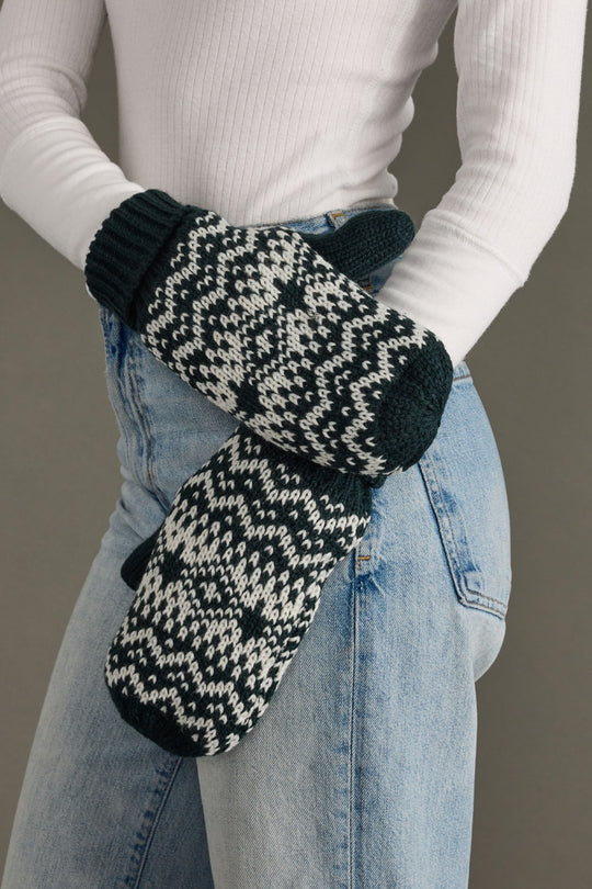 Person wearing dark teal and white patterned mittens with a plain background