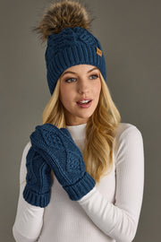 Woman wearing a blue knitted hat with a pom-pom and matching mittens against a gray background