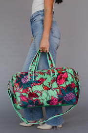 Person holding a colorful floral-patterned duffel bag against a gray background