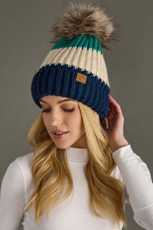 Woman wearing a multicolored knit beanie with a pom-pom against a neutral background