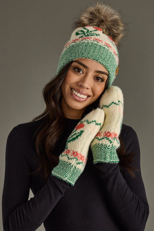 Woman wearing a green and beige knit hat and mittens with a floral pattern on a gray background