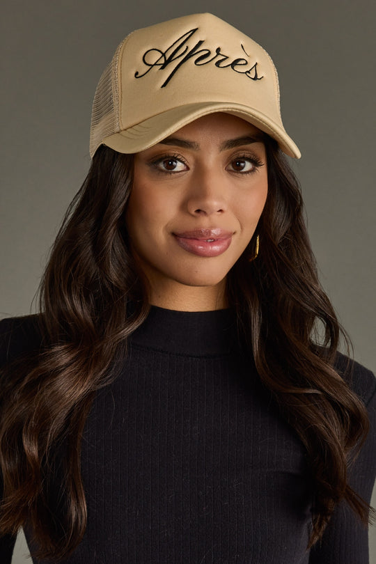 Woman wearing a beige cap with 'Apres' text against a gray background