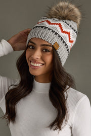 Woman wearing a gray knit beanie with a fur pom-pom against a neutral background