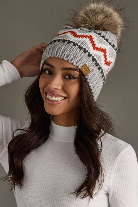 Woman wearing a gray knit beanie with a fur pom-pom against a neutral background