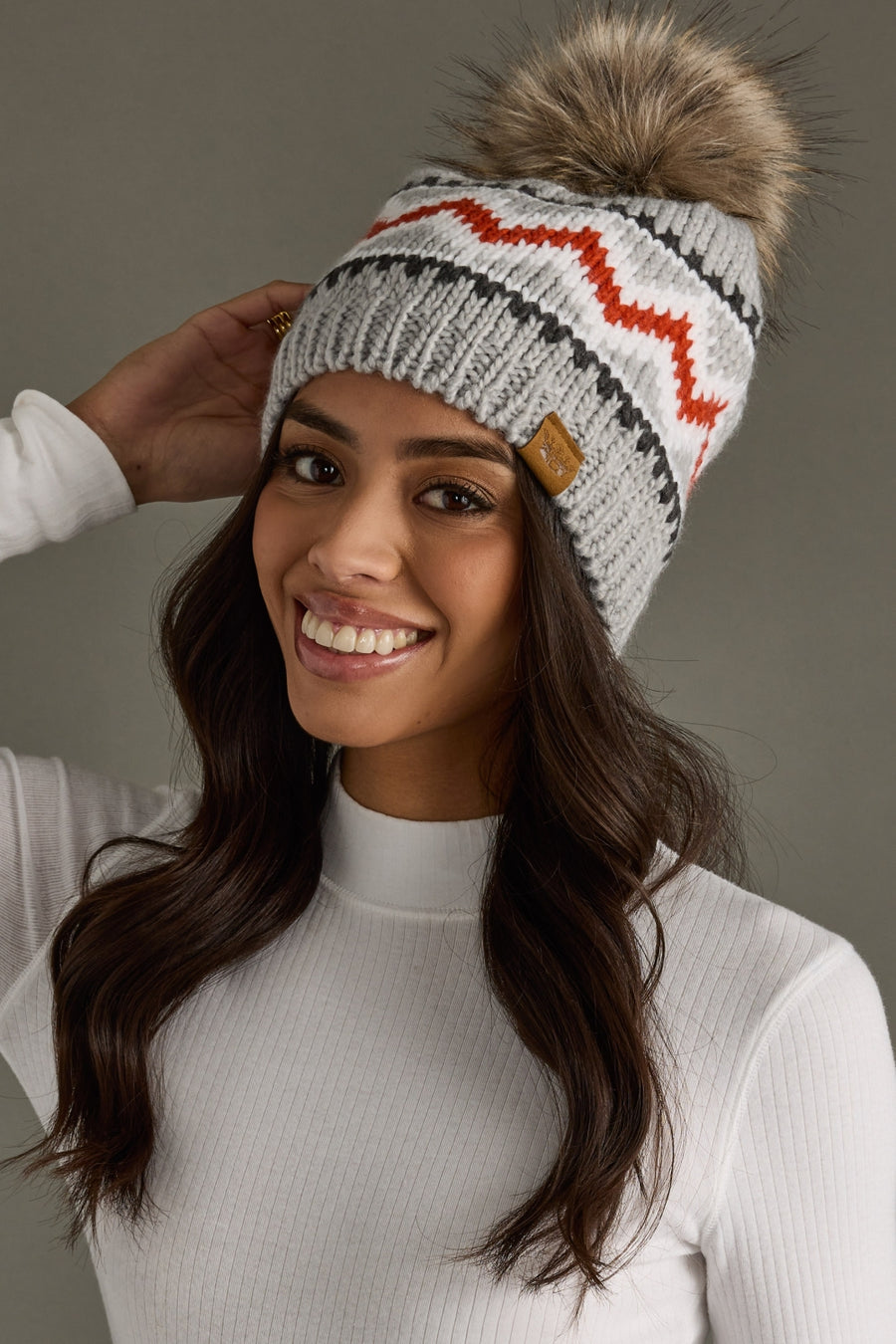 Woman wearing a gray knit beanie with a fur pom-pom against a neutral background