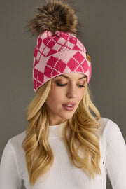 Woman wearing a pink and blush argyle beanie with a fur pom-pom on a gray background
