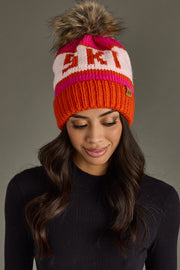 Person wearing a colorful knit beanie with a pom-pom on a gray background