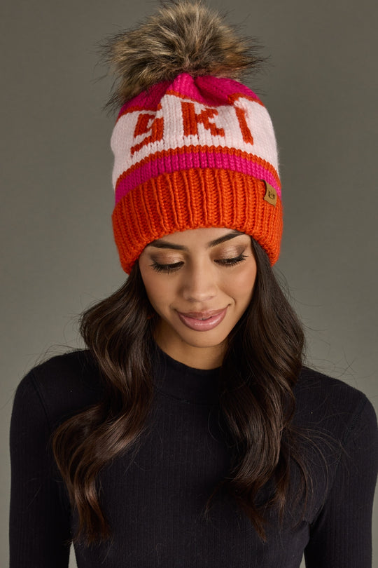 Person wearing a colorful knit beanie with a pom-pom on a gray background